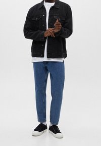 Chaqueta de mezclilla negra con bolsillos delanteros, camiseta blanca debajo, jeans rectos de tono azul claro y zapatillas negras con suela blanca.