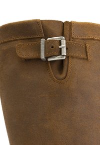 Botte en daim marron avec une boucle en métal argenté et un détail de sangle près du bord supérieur.