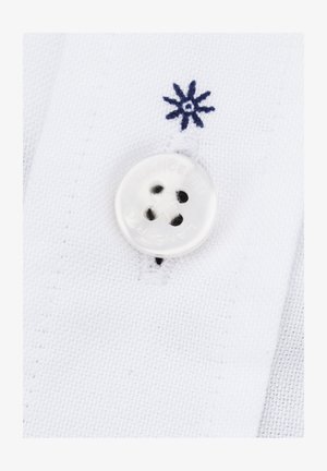 Biała tkanina o teksturze przędzy, z białym guzikiem na cztery dziurki i w pobliżu haftowanym detalem kwiatowym w kolorze granatowym.