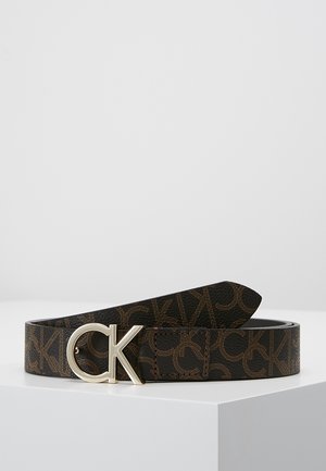 Bruine leren riem met herhalend "CK" patroon en metalen gesp met "CK" logo, getoond opgerold op een witte ondergrond tegen een effen achtergrond.