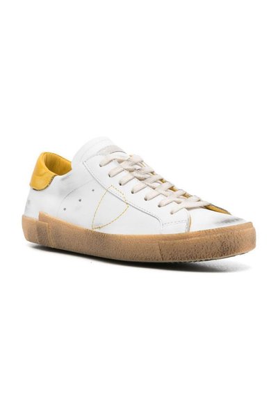 Sneaker bianche in pelle con un accento giallo sul tallone, lacci beige e suola in gomma testurizzata. Presentano cuciture sottili e perforazioni laterali.