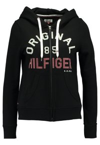 Svart zip-up hoodie med texten "Original 85 Hilfiger" i vitt och burgundy, med huva med dragsko och framfickor. Slät textur.