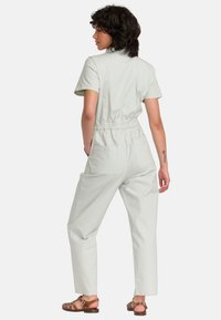 Lichtgroene jumpsuit met korte mouwen, elastische taille en twee achterzakken, ontworpen met een relaxte pasvorm en rechte pijpen.