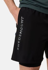 Zwarte sportshorts van lichtgewicht stof, met "SWEDEMOUNT" in reflecterende opdruk langs de zijkant en een klein Zweeds vlagdetail.