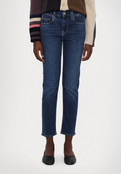 Jeans din denim de culoare albastru închis, cu o croială dreaptă, talie medie, cinci buzunare și tiv desfăcut. Purtați cu pantofi plat negru.
