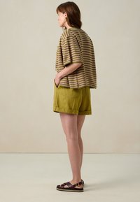 Haut en tricot rayé dans des tons de marron et de rose, associé à un short en lin olive. Sandales noires et marron avec un détail boucle. Design minimaliste.