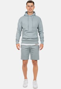 Lichtgrijze hoodie met trekkoorden en een voorzak, gecombineerd met bijpassende shorts. Zachte stof, minimale branding op de tailleband en comfortabele pasvorm.