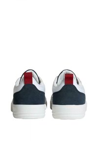 Baskets blanches avec un dos en suède bleu marine et une tirette rouge. Présentent une forme lisse et arrondie ainsi qu'une semelle en caoutchouc blanc texturé.