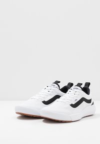 Białe sportowe sneakersy z czarnymi akcentami, wykonane z teksturowanego materiału siateczkowego, z wyściełanym kołnierzem i żłobioną gumową podeszwą dla lepszej przyczepności.
