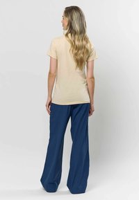 Beige színű, rövid ujjú póló, amely laza szabású sötétkék nadrággal van párosítva, kiemelve a kényelmes dizájnt és a sima anyag textúráját.