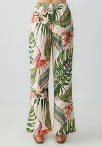 Pantaloni a gamba larga floreali con uno sfondo crema e colorati motivi di foglie e fiori tropicali, cinturino elastico e texture liscia.