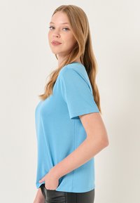 Lichtblauwe korte mouwen T-shirt van zachte, gladde stof; heeft een ontspannen pasvorm en subtiele zijnaden, gestyled met zwarte broeken.