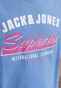 Blå bomulds t-shirt med hvid og pink grafisk tekst, "JACK & JONES," "Superior," og "INTERNATIONAL STANDARD."