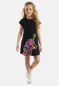 Schwarzes Baumwoll-T-Shirt-Kleid mit einem bunten Einhorn-Design, das mit Farbspritzern in Pink, Lila und Gelb auf einem einfarbigen Hintergrund versehen ist.