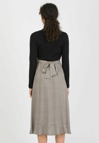 Schwarzes, geripptes Langarmtop, kombiniert mit einem gemusterten Rock, der eine Taillenschnürung und einen ausgestellten Saum im beigen und braunen geometrischen Design aufweist.