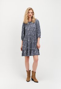 Sukienka w kwiaty, granatowa, z rękawami trzy czwarte i rozkloszowanym dołem. Noszona z beżowymi kowbojkami z haftem i obcasem.