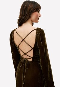 Robe en velours vert foncé à manches longues, avec un col froncé et un détail de lien croisé dans le dos. Texture lisse et silhouette ajustée.