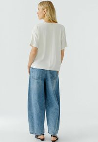 Korte mouwen, crèmekleurige blouse met een gladde textuur, gecombineerd met wijde, blauwe spijkerbroeken met achterzakken en een relaxte pasvorm.