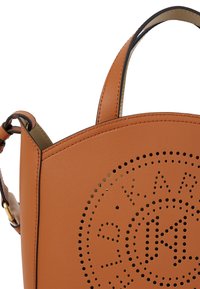 Bruine leren handtas met geperforeerd cirkelontwerp en logo, voorzien van dubbele handvatten en een gladde textuur. Gouden accenten zichtbaar.