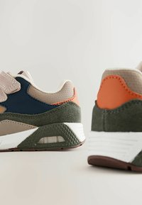 Sneakers featuring mixed materials: beige mesh, navy panel, orange accent, olive green suede, white midsole, textured rubber outsole.