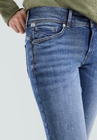 Vervaagde blauwe denim spijkerbroek met een slim fit, vijf zakken en contrasterende stiksels. Heeft een klein label op de tailleband.