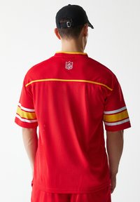 Piros NFL mez sárga díszítéssel, hálós anyagból, rövid ujjú, sárga és fehér vízszintes csíkokkal. Logó a hát felső részén.