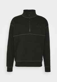 Sudadera negra con cuello de media cremallera, bolsillo frontal y detalles de costuras grises. Presenta un logotipo discreto en el pecho. Material suave de polar.