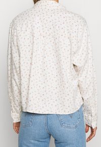 Chemise à manches longues en coton blanc avec un petit imprimé floral. Dotée d'un col, de poignets à boutons et d'une coupe ample avec un ourlet arrondi.