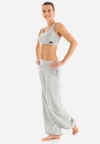 Grauer Sport-BH mit einem Logo, kombiniert mit lockeren grauen Sweatpants mit Kordelzug und Bündchen. Glattes Material und taillierter Schnitt.