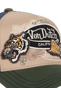 Beige Kappe mit grünem Schirm, versehen mit gestickten Tiger- und Flügel-Patches sowie einem schwarzen "Von Dutch California"-Logo. Strukturiertes Gewebe-Design.