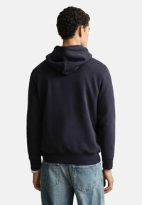 Marineblaue Kapuzenjacke mit weicher Textur, gerippten Bündchen und einem Taillenbund. Sichtbare Nähte auf der Rückseite.