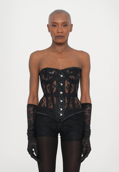 Corset en dentelle noire sans bretelles, avec fermeture à crochets sur le devant et bonnets structurés. Des gants en dentelle assortis et un short complètent le look.