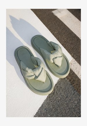 Egy pár zöld párnázott flip-flop fekete-fehér csíkos gyalogátkelőhelyen, aszfaltburkolaton.