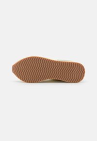 Hardloopschoen zool met bruine rubber en zigzag profiel, licht gebogen hak en teen, op een effen witte achtergrond.