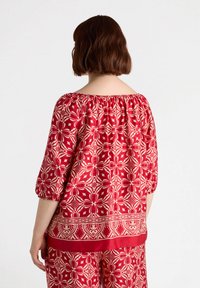 Blusa rossa con motivo a fiori, design off-the-shoulder, scollo elastico e maniche a tre quarti a palloncino, caratterizzata da intricati motivi floreali.