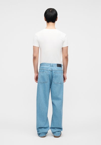 Ανοιχτό μπλε τζιν με άνετη εφαρμογή, διαθέτει δύο πίσω τσέπες και μαύρο έμπλαστρο στη μέση. Φοριέται με εφαρμοστή λευκή μπλούζα.