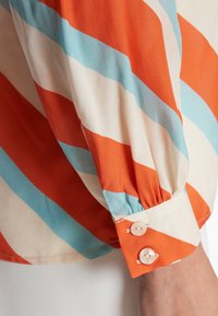 Kurzärmelige Bluse in orange, blau und cremefarbenen Streifen; verfügt über einen geknöpften Bund mit zwei Perlenknöpfen und gerafften Ärmel-Details.