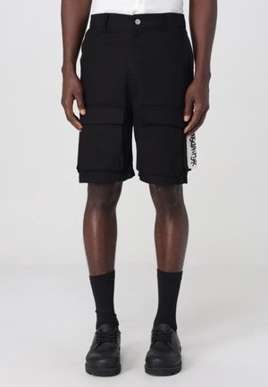 Pantaloni cargo neri realizzati in tessuto testurizzato, con due ampie tasche laterali e una piccola etichetta grafica sulla cucitura laterale.