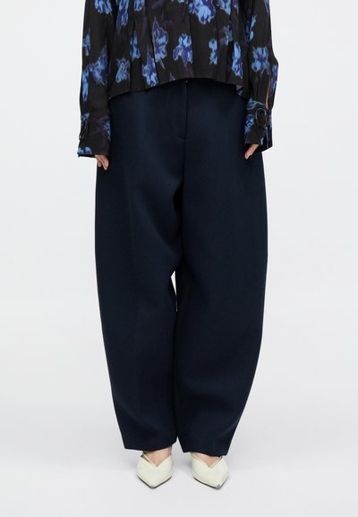 Navyblå bukser med vide ben i blødt stof, der har høj talje og struktureret silhuet. Kombination med en sort blomsterbluse.
