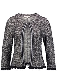 Svart och vit texturerad jacka med öppen front, fransad fåll och kontrasterande kant längs kanterna. Tillverkad av bouclétyg.