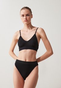 Set negru din două piese, format dintr-un bralette cu decolteu adânc în V și bretele subțiri, împreună cu chiloți înalți, asortați, confecționați dintr-un material neted și elastic.