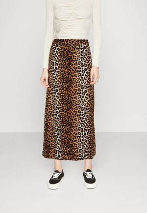 Woman wearing a long leopard print skirt, cream ruched long-sleeve top, and black sneakers with white laces against plain background.