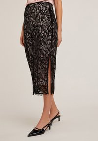Zwarte kant midi-rok met intrikate patronen en zijsplitsen. De afgeknipte zoom heeft een franjesrand. Gekocht met een satijnen roze top en zwarte hakken.
