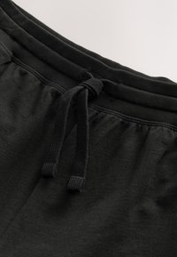 Pantaloni sport negri din bumbac, cu talie elastică și șnur ajustabil. Țesătura are o textură fină, cu detalii minime de cusături.