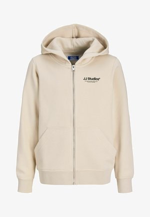 Bežinė užtrauktuku užsegama megztinė, pagaminta iš minkštos medžiagos, su priekiniais užtrauktuku, dviem šoninėmis kišenėmis ir logotipu, atspausdintu kairėje krūtinės pusėje.