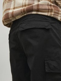 Schwarze Cargo-Hosen haben eine glatte Textur, mit einer Gesäßtasche und dezenten Stichdetails. Kombiniert mit einem karierten Hemd in Braun und Creme.