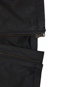 Giacca di pelle nera con due tasche con zip visibili. La texture è liscia con un aspetto leggermente rugoso. La minuteria della zip è in bronzo.