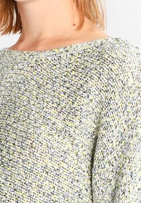 Maglione lavorato a maglia con una vestibilità ampia, scollatura a barca e texture varia con sfumature di grigio, giallo e verde. Tessuto leggero e traspirante.