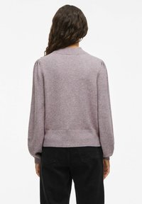 Maglione lavorato a maglia di un leggero viola, con collo tondo, maniche a sbuffo e orlo a costine, abbinato a pantaloni neri. Tessuto morbido e vestibilità casual.