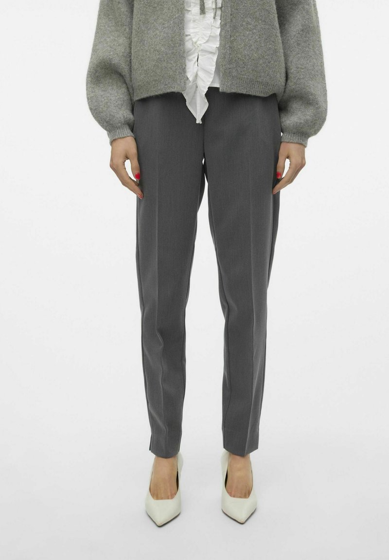Pantaloni grigi su misura con taglio dritto e piega frontale, abbinati a una blusa bianca testurizzata e a un cardigan di maglia grigio chiaro.